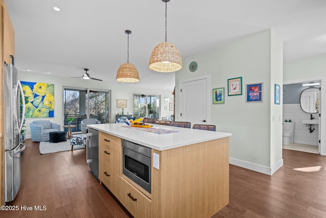 kitchen featuring dark wood-type flooring, hanging light fixtures, stainless steel appliances, a center island, and light brown cabinetry