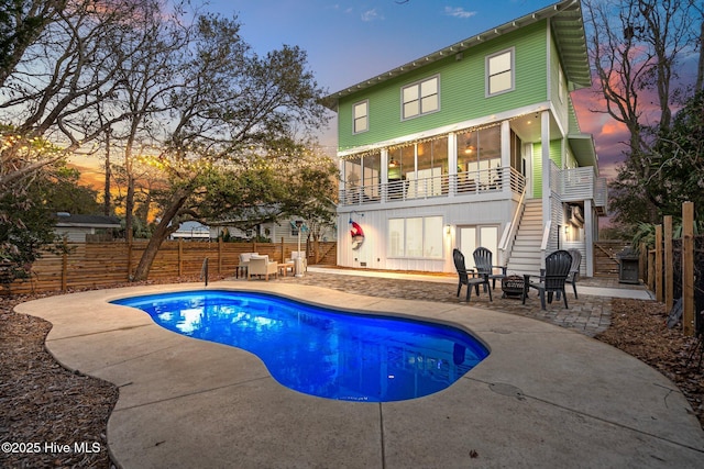 back house at dusk featuring a fenced in pool, a patio, a balcony, and an outdoor fire pit