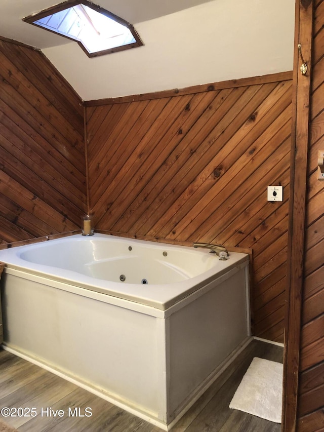 bathroom with wooden walls, a jetted tub, a skylight, and wood finished floors