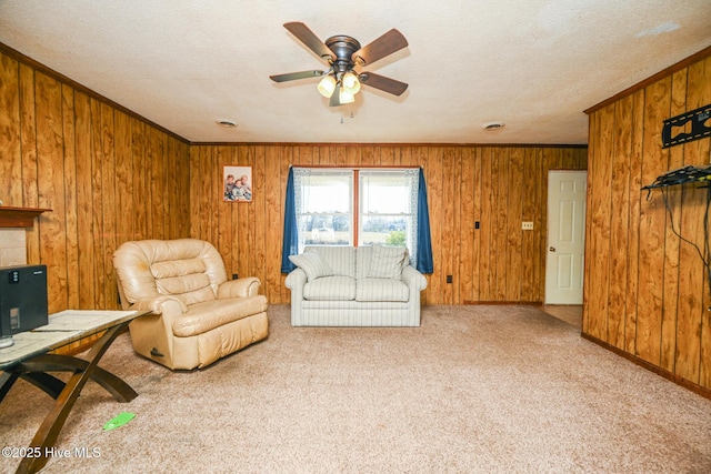 carpeted living room with a fireplace, wooden walls, ornamental molding, and ceiling fan