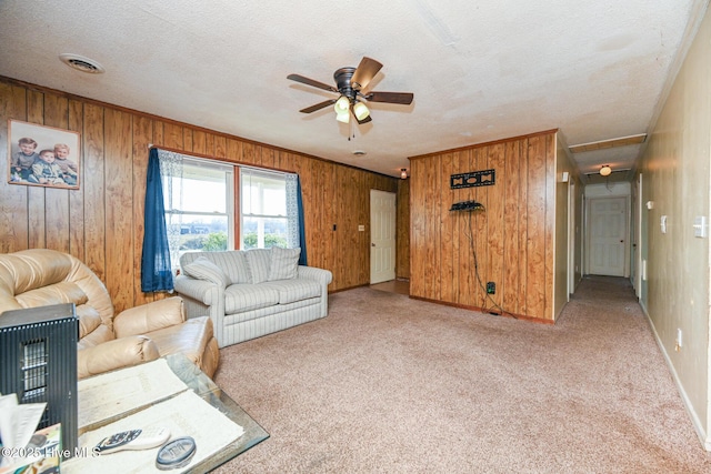 carpeted living room with crown molding, ceiling fan, a textured ceiling, and wood walls