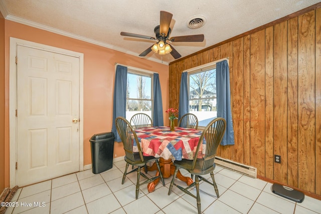 dining room with baseboard heating, ornamental molding, a textured ceiling, and wood walls