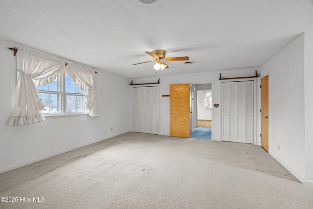 unfurnished bedroom featuring multiple closets, ceiling fan, carpet, and a textured ceiling