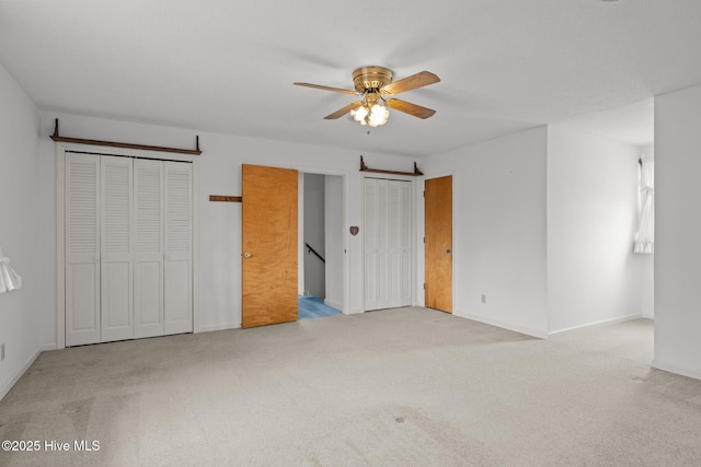 unfurnished bedroom with two closets, light colored carpet, and ceiling fan