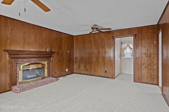 unfurnished living room with ceiling fan, wooden walls, light colored carpet, and a fireplace