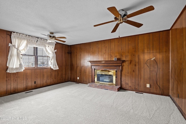 unfurnished living room with a textured ceiling, wooden walls, carpet flooring, ceiling fan, and a fireplace