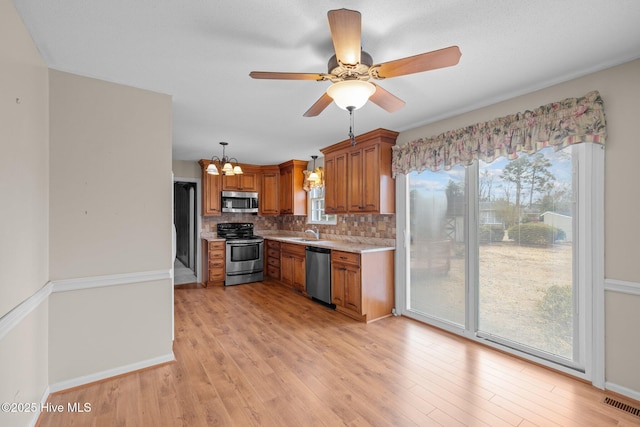 kitchen featuring sink, backsplash, hanging light fixtures, stainless steel appliances, and light hardwood / wood-style floors