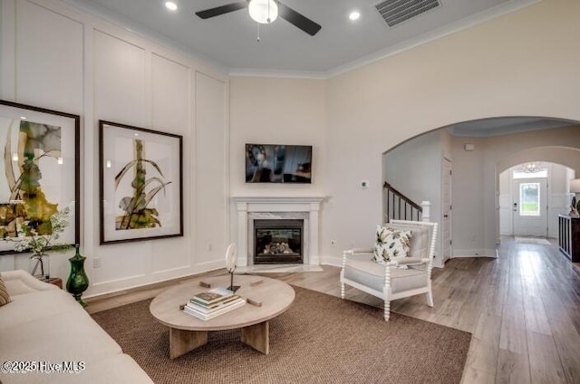 living room with hardwood / wood-style flooring, ceiling fan, ornamental molding, and a high end fireplace