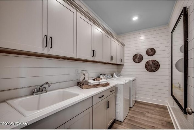 laundry room with sink, wood walls, cabinets, washer and clothes dryer, and light hardwood / wood-style floors