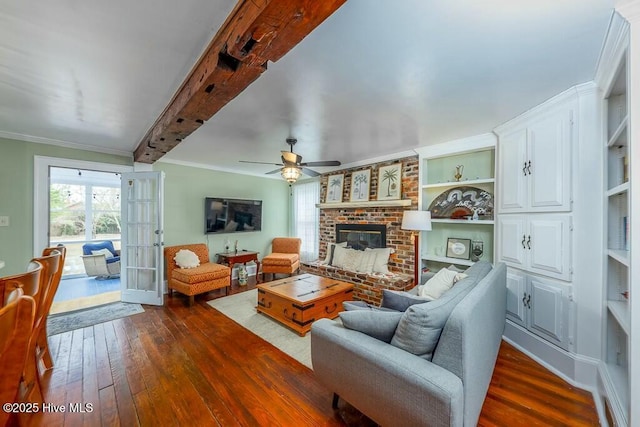 living room with dark hardwood / wood-style floors, beamed ceiling, crown molding, a brick fireplace, and french doors