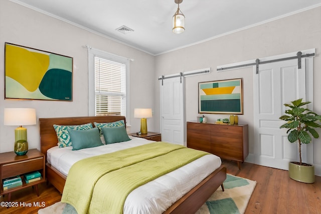 bedroom featuring hardwood / wood-style floors, crown molding, and a barn door