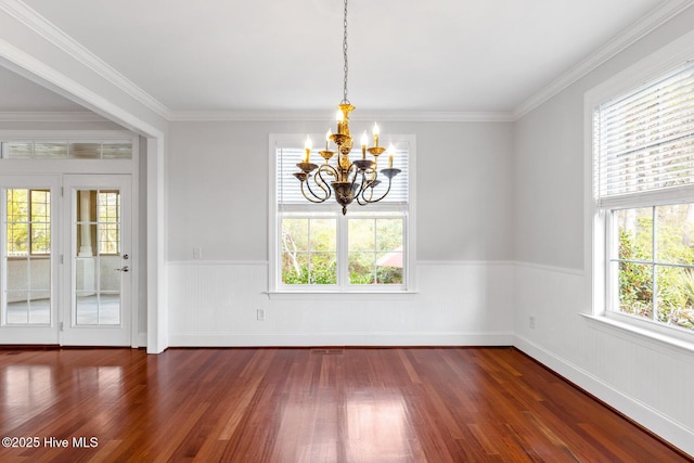 unfurnished dining area featuring crown molding, a healthy amount of sunlight, dark hardwood / wood-style flooring, and a chandelier