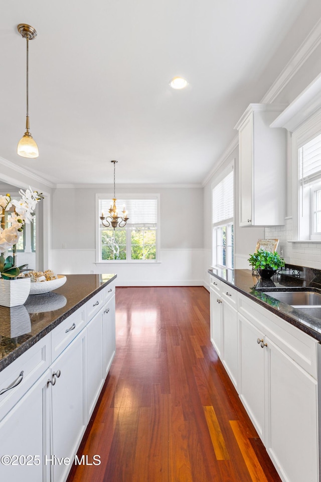 kitchen featuring dark stone countertops, hanging light fixtures, crown molding, and white cabinets