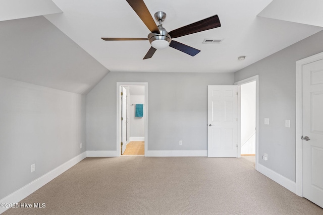 unfurnished bedroom featuring vaulted ceiling, connected bathroom, light colored carpet, and ceiling fan