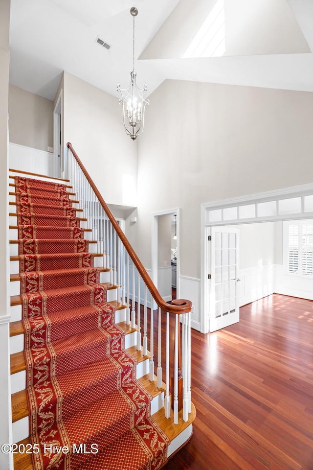 stairway with an inviting chandelier, hardwood / wood-style flooring, and high vaulted ceiling