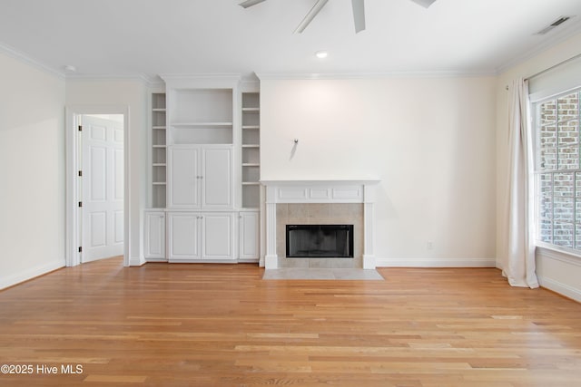 unfurnished living room featuring built in shelves, crown molding, light wood-type flooring, ceiling fan, and a fireplace