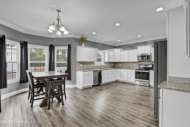 kitchen with sink, white cabinetry, stainless steel appliances, decorative backsplash, and decorative light fixtures