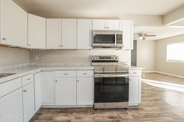 kitchen featuring ceiling fan, stainless steel appliances, wood-type flooring, a textured ceiling, and white cabinets