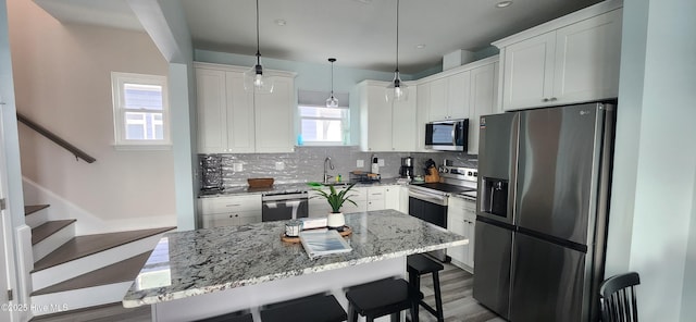 kitchen featuring appliances with stainless steel finishes, white cabinetry, hanging light fixtures, a center island, and a kitchen bar