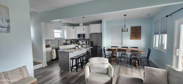 kitchen with white cabinetry, a center island, hanging light fixtures, appliances with stainless steel finishes, and light stone countertops