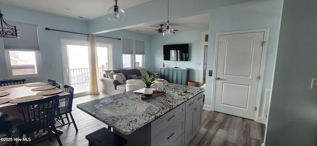 kitchen featuring pendant lighting, dark wood-type flooring, ceiling fan, light stone counters, and a kitchen island