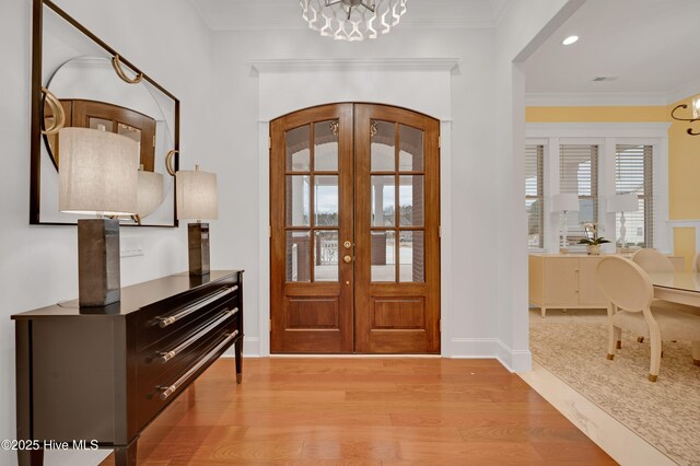 foyer entrance featuring crown molding, light hardwood / wood-style floors, french doors, and a chandelier