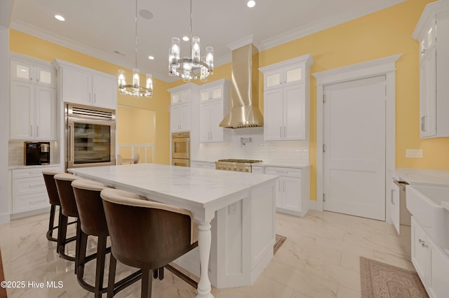 kitchen with white cabinetry, ornamental molding, wall chimney exhaust hood, and a center island