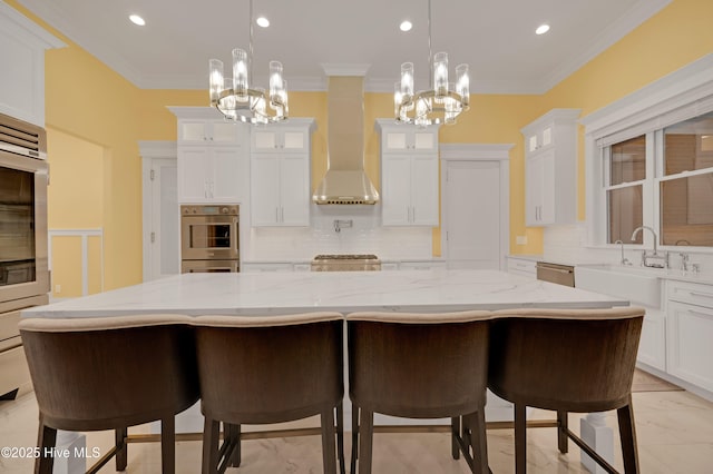 kitchen with pendant lighting, white cabinetry, a kitchen bar, wall chimney range hood, and a spacious island