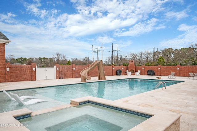 view of swimming pool with a water slide, a patio, and an in ground hot tub