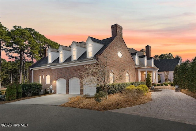 view of front of property featuring a garage, brick siding, driveway, and a chimney