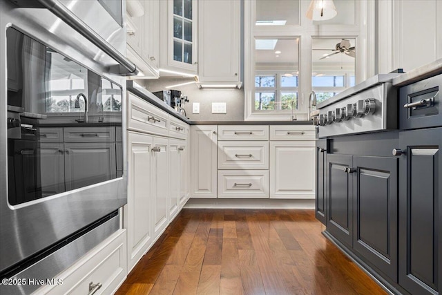 kitchen with dark countertops, glass insert cabinets, dark wood-type flooring, white cabinets, and a sink