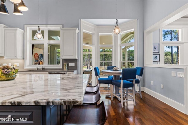 bar with baseboards, dishwashing machine, dark wood-type flooring, a sink, and decorative light fixtures