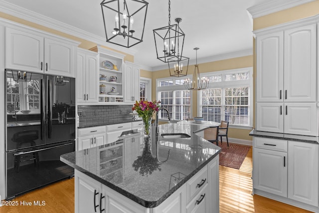 kitchen featuring pendant lighting, white cabinetry, dark stone countertops, black fridge, and a center island with sink