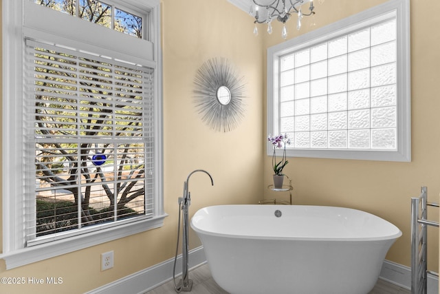 bathroom featuring a wealth of natural light, an inviting chandelier, and a tub to relax in