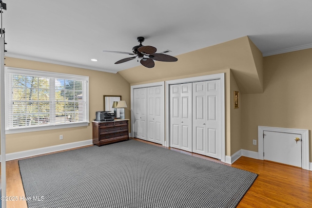 unfurnished bedroom with vaulted ceiling, ceiling fan, hardwood / wood-style floors, and two closets