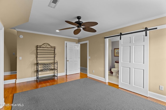 unfurnished bedroom with ornamental molding, a barn door, connected bathroom, and hardwood / wood-style floors