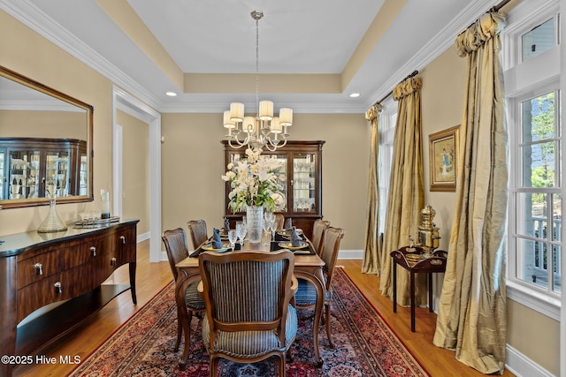 dining space with a raised ceiling, wood-type flooring, ornamental molding, and an inviting chandelier