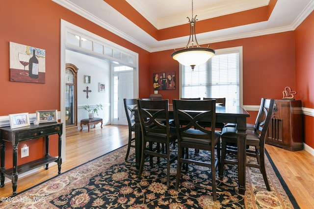 dining room featuring crown molding, a tray ceiling, and light hardwood / wood-style floors