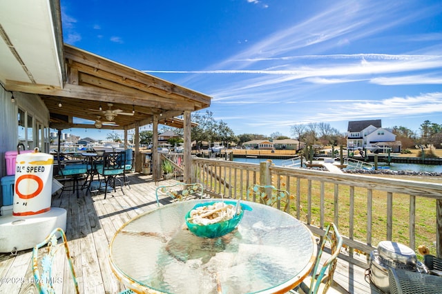 wooden deck featuring a ceiling fan, outdoor dining space, and a water view