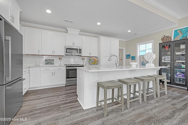 kitchen featuring a kitchen bar, sink, appliances with stainless steel finishes, a kitchen island with sink, and white cabinets