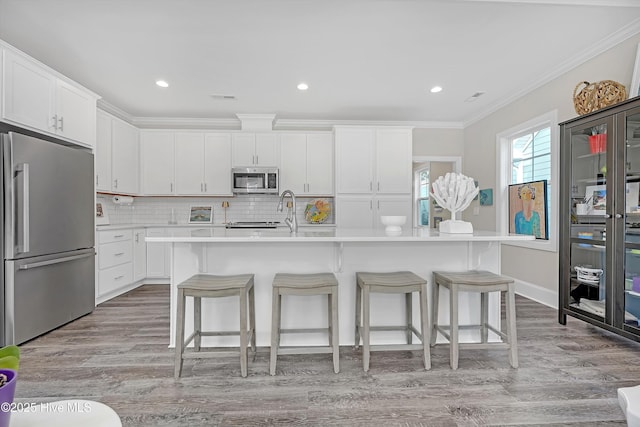 kitchen with white cabinetry, crown molding, a kitchen breakfast bar, an island with sink, and stainless steel appliances