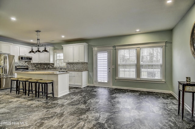 kitchen with sink, white cabinetry, a center island, hanging light fixtures, and stainless steel appliances