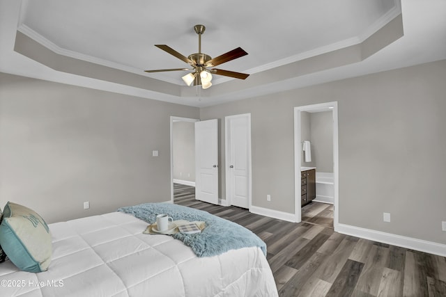 bedroom featuring crown molding, dark wood-type flooring, ensuite bath, and a tray ceiling