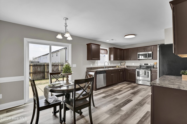 kitchen with dark brown cabinetry, appliances with stainless steel finishes, decorative light fixtures, and light hardwood / wood-style flooring