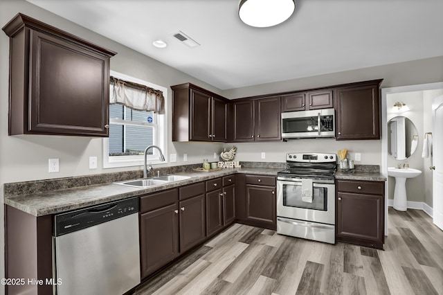 kitchen featuring stainless steel appliances, sink, dark brown cabinetry, and light wood-type flooring