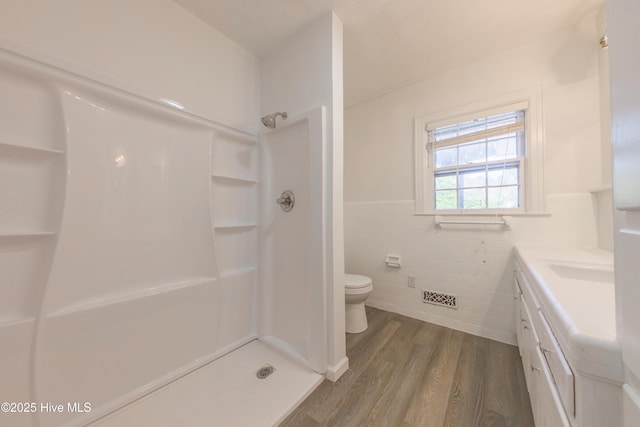 bathroom featuring tile walls, vanity, wood-type flooring, toilet, and walk in shower