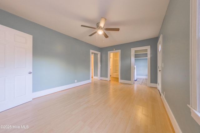 unfurnished bedroom with ceiling fan, connected bathroom, a walk in closet, a closet, and light wood-type flooring