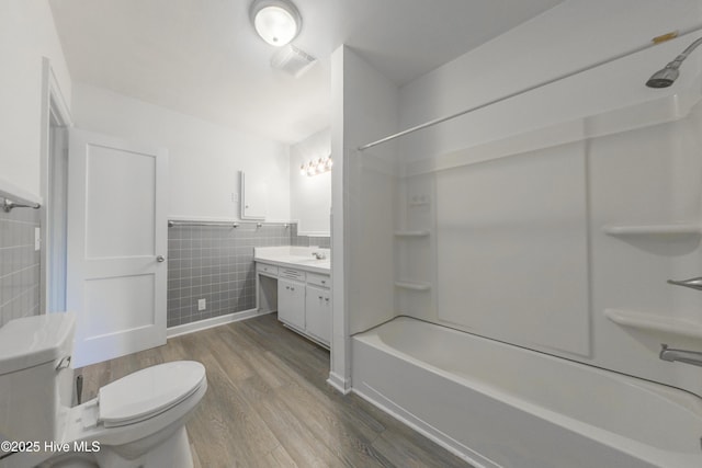 full bathroom with hardwood / wood-style flooring, tile walls, vanity, shower / bathing tub combination, and toilet