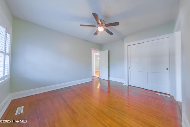 unfurnished bedroom with multiple windows, wood-type flooring, ceiling fan, and a closet