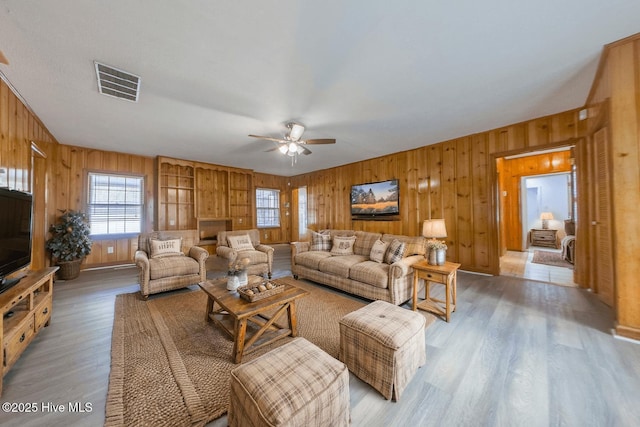 living room with ceiling fan, light wood-type flooring, and wood walls